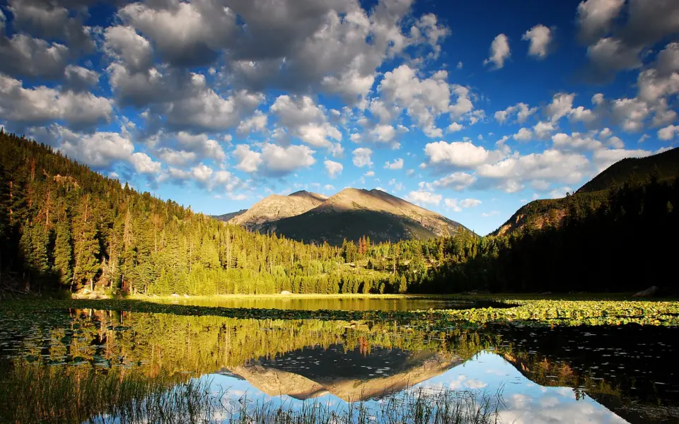 A still lake at dawn mirroring green hills and a mountain under a cloudy sky